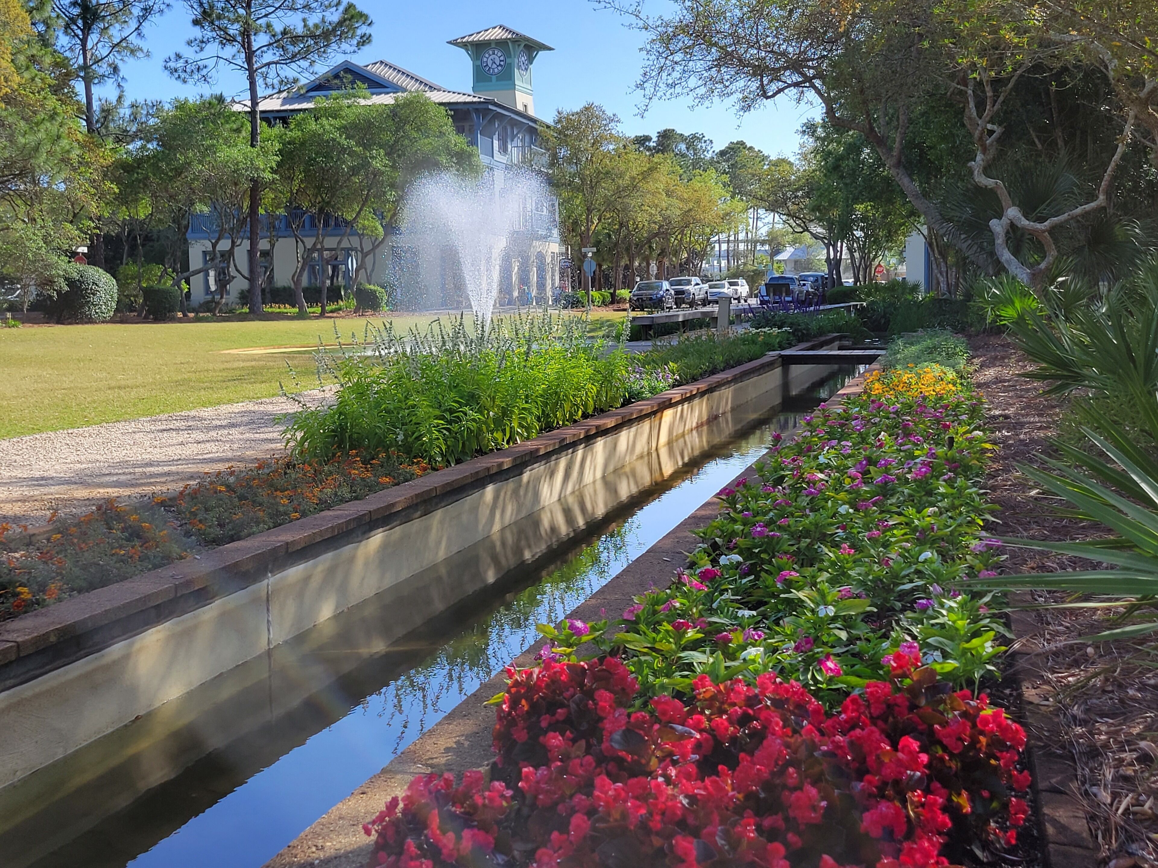 A garden with a water feature, a pathway, and a building with a clock tower.