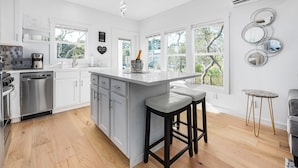 Een moderne keuken met witte kasten, een centraal eiland met krukken, een koffieapparaat en een vaatwasser.