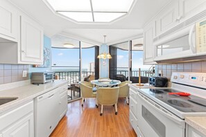 A modern kitchen with a dining area, large windows, and a view of the city.