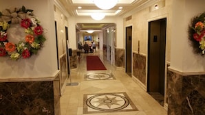 A hallway with marble floors, a red carpet, and floral decorations on the walls.
