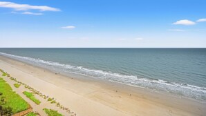 A beach with a clear sky, sandy shore, and a few people walking. - Regency Towers 1602 -Pool & Hot Tub Year-Round (Myrtle Beach)