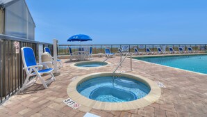 A pool area with two hot tubs, lounge chairs, and a blue umbrella. - Regency Towers 1602 -Pool & Hot Tub Year-Round (Myrtle Beach)