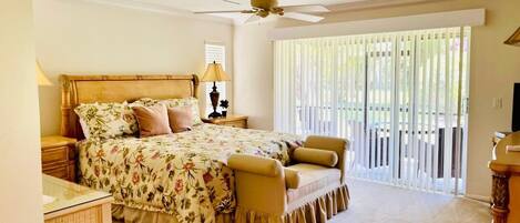 A bedroom with a bed, bedside tables, a lamp, a ceiling fan, and a view through a window with blinds.
