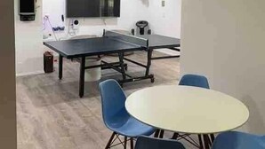 A modern room with a ping pong table, blue chairs, a white table, and a mounted deer head.
