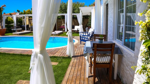 A wooden deck with a pool, outdoor seating, and a covered area with white curtains. - Rikas Alacati (Cesme)