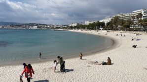 A beach with people, a clear sky, and buildings in the background.