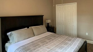 Une chambre à coucher avec une tête de lit sombre, une couvre-lit à motifs, un ventilateur de plafond et une porte blanche.