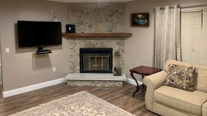 Un salon avec une cheminée, un téléviseur, un ventilateur de plafond et un canapé.