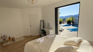 Un dormitorio con una cama grande, un escritorio y vistas a una piscina y montañas.