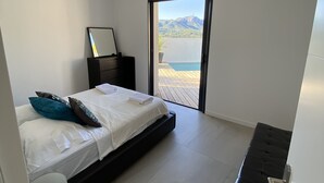 Un dormitorio moderno con una cama, mesita de noche y vistas a un balcón con montaña y agua.