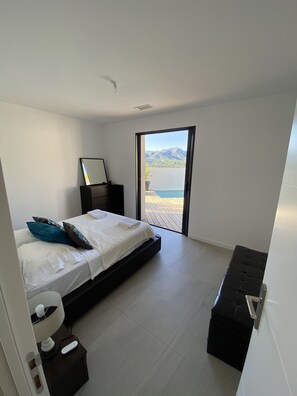 Et moderne soveværelse med seng, sengebord og udsigt til en balkon med bjerg og vand.