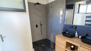 Un baño moderno con cabina de ducha de vidrio, tocador de madera con lavamanos negros y un espejo grande.
