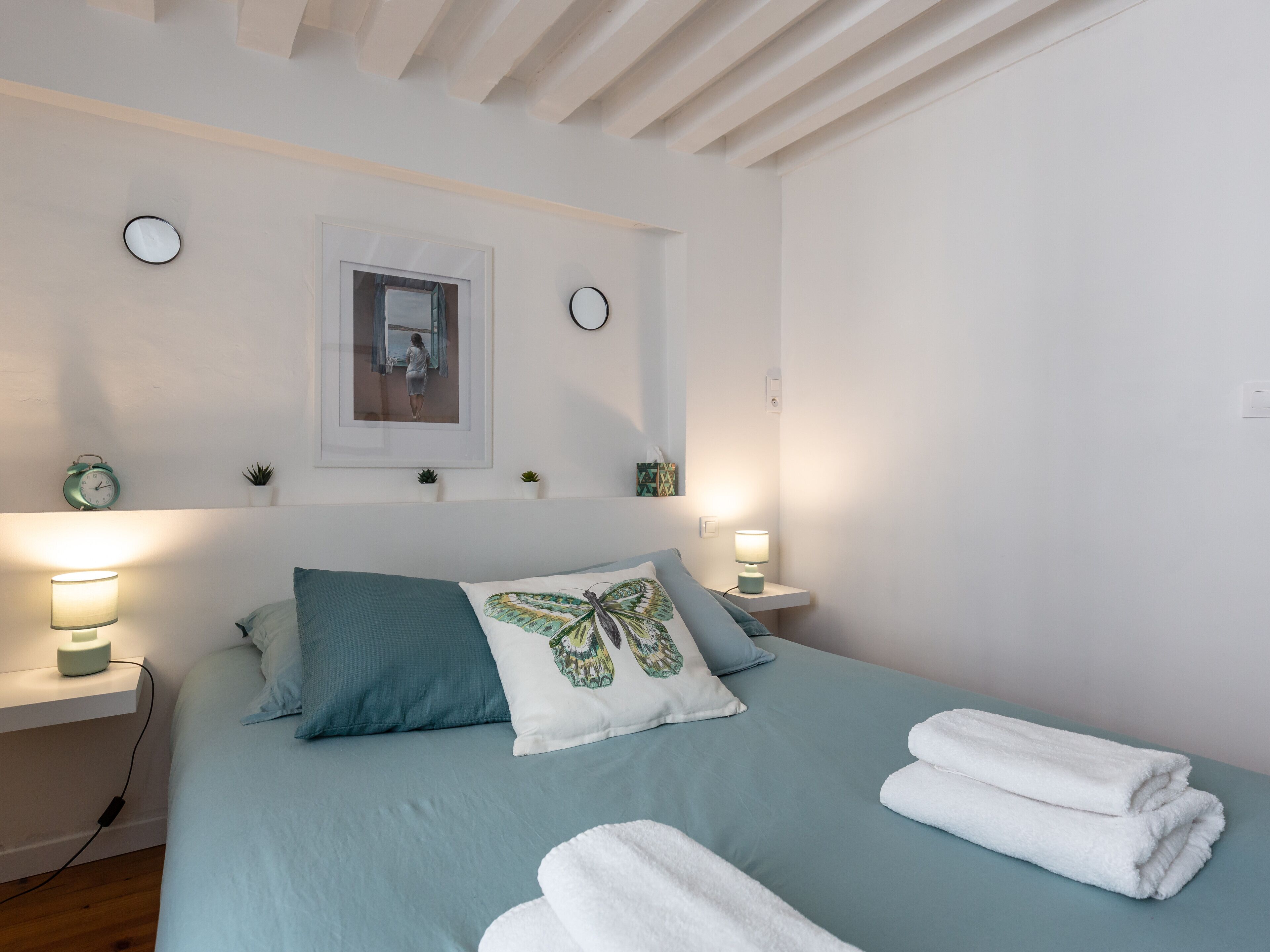 A neatly made bed with blue bedding and white towels, a framed picture on the wall, and bedside lamps.