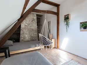 A loft bedroom with exposed wooden beams, a stone wall, a hanging chair, and a small plant.