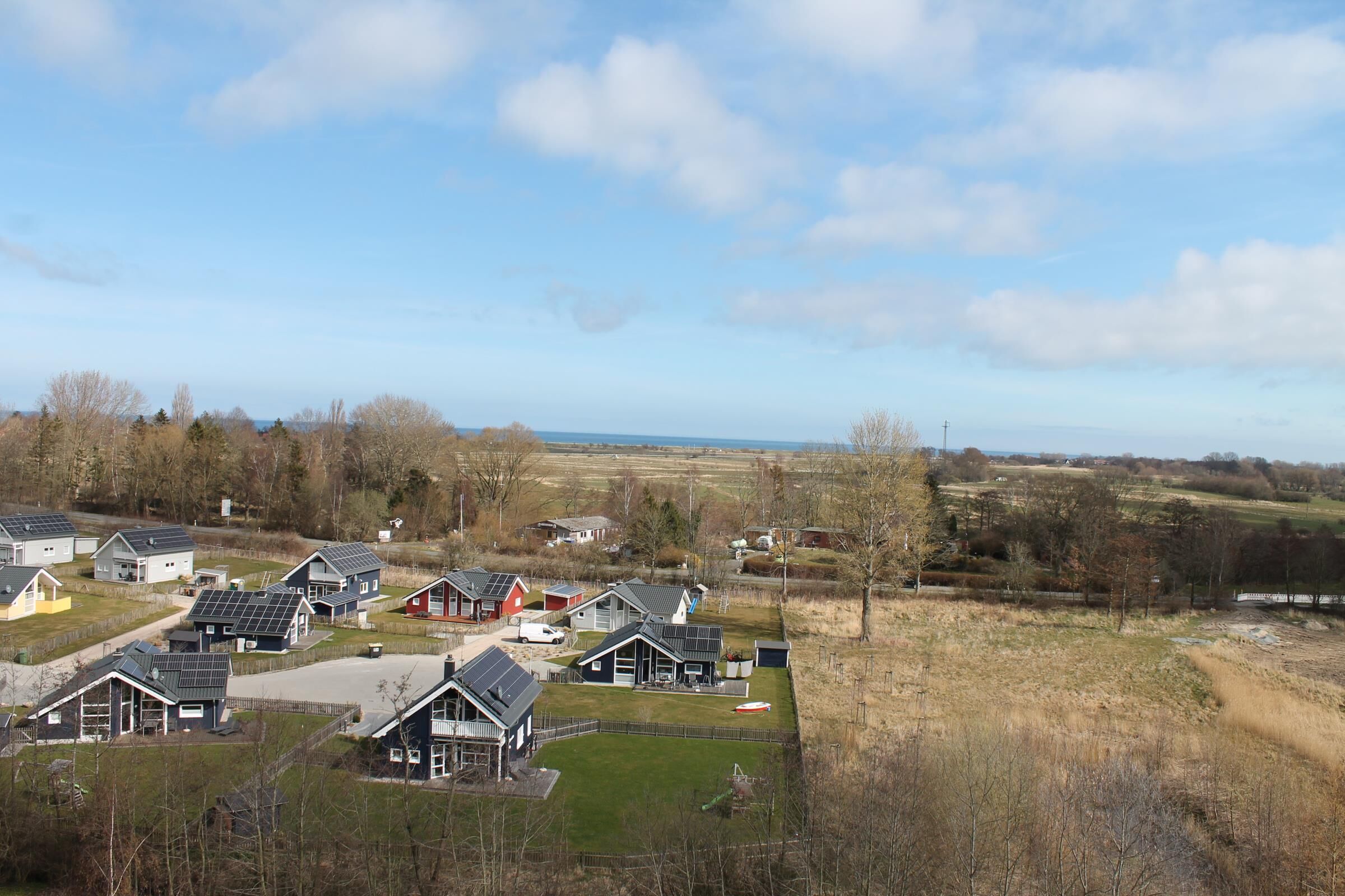 A residential area with houses featuring solar panels, a clear sky, and a distant view of the sea.