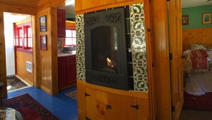 Een gezellig houten blokhut interieur met een centraal gelegen open haard, houten wanden en een raam met rode lijst.