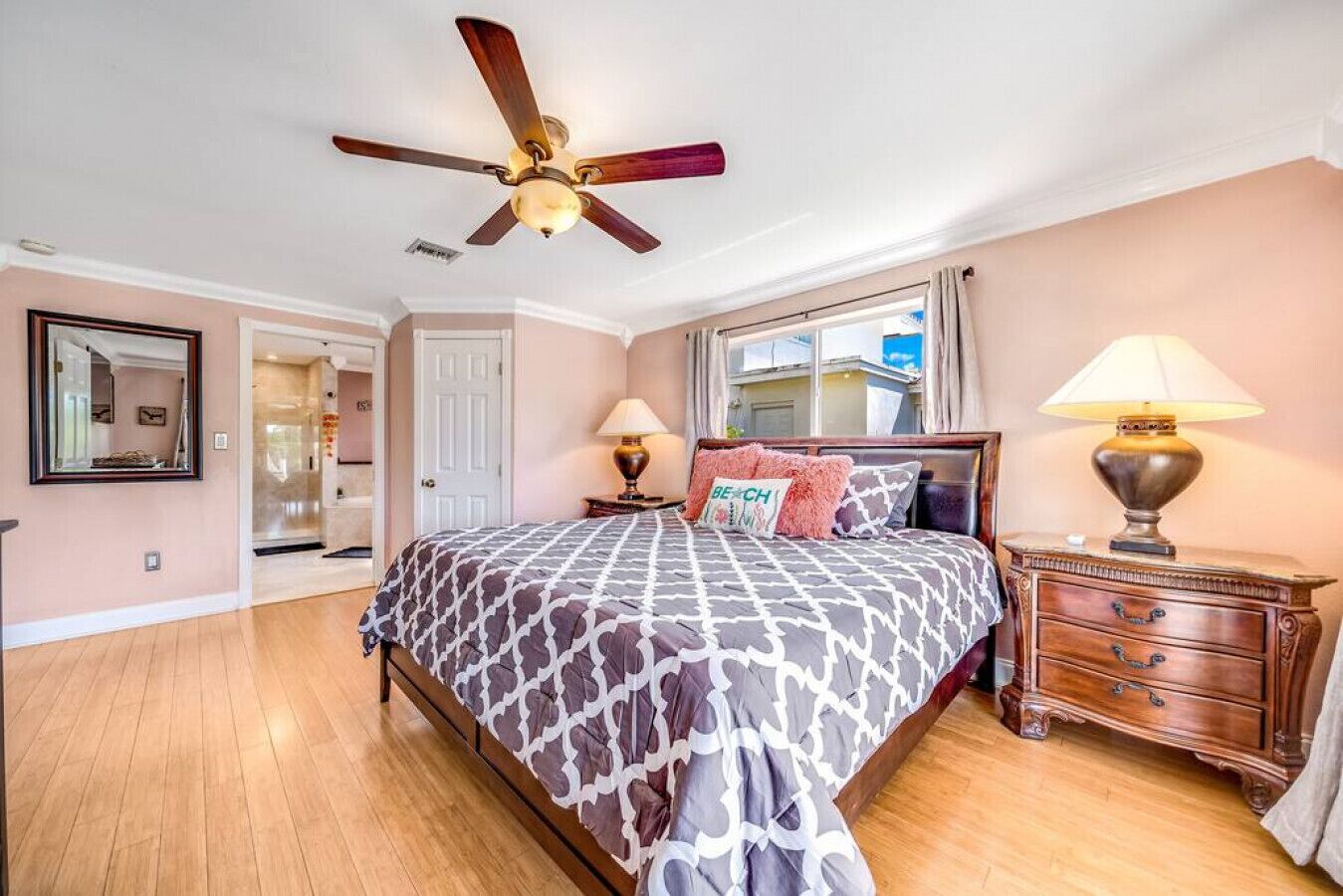 Une chambre avec un grand lit, un ventilateur de plafond, une table de chevet avec une lampe et une vue sur l’extérieur.