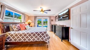Un dormitorio con cama, ventilador de techo, escritorio y vista al exterior.