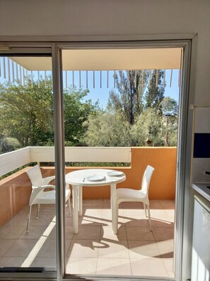 Un balcon avec une table ronde et quatre chaises, une porte-fenêtre coulissante et une vue sur les arbres et les collines.