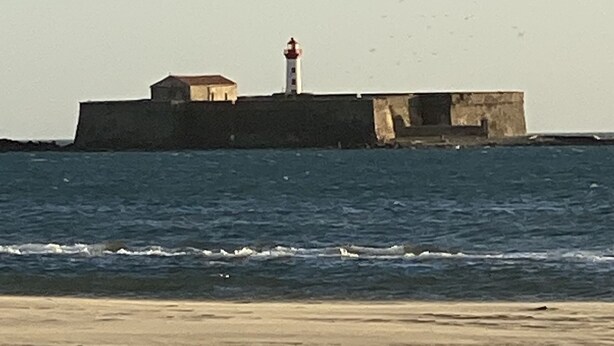 Escena costanera amb un far sobre una estructura de pedra, ones que s'acosten a la riba i una platja sorrenca.