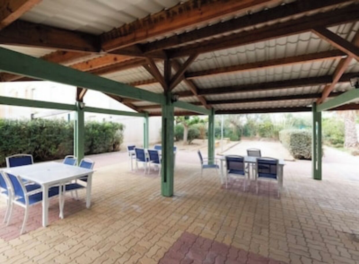 An outdoor covered patio area with tables and chairs, surrounded by greenery.