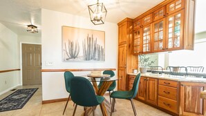 A dining area with a round table, four chairs, wooden cabinets, and a kitchen counter. - Spacious 3BR Extended Stay: Airport, Downtown, Ski (North Salt Lake)