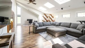 A modern living room with a sectional sofa, a desk with a computer, and a ceiling fan. - Modern, Magical Woodsy Escape 1 Hour From NYC (Putnam Valley)