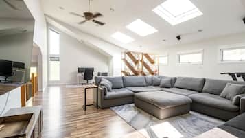Un salon moderne avec un canapé d’angle, un bureau avec un ordinateur et un ventilateur de plafond.