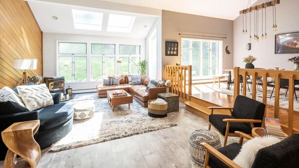 A spacious living room with a large sectional sofa, a coffee table, and a dining area with wooden chairs and a table. - Modern, Magical Woodsy Escape 1 Hour From NYC (Putnam Valley)