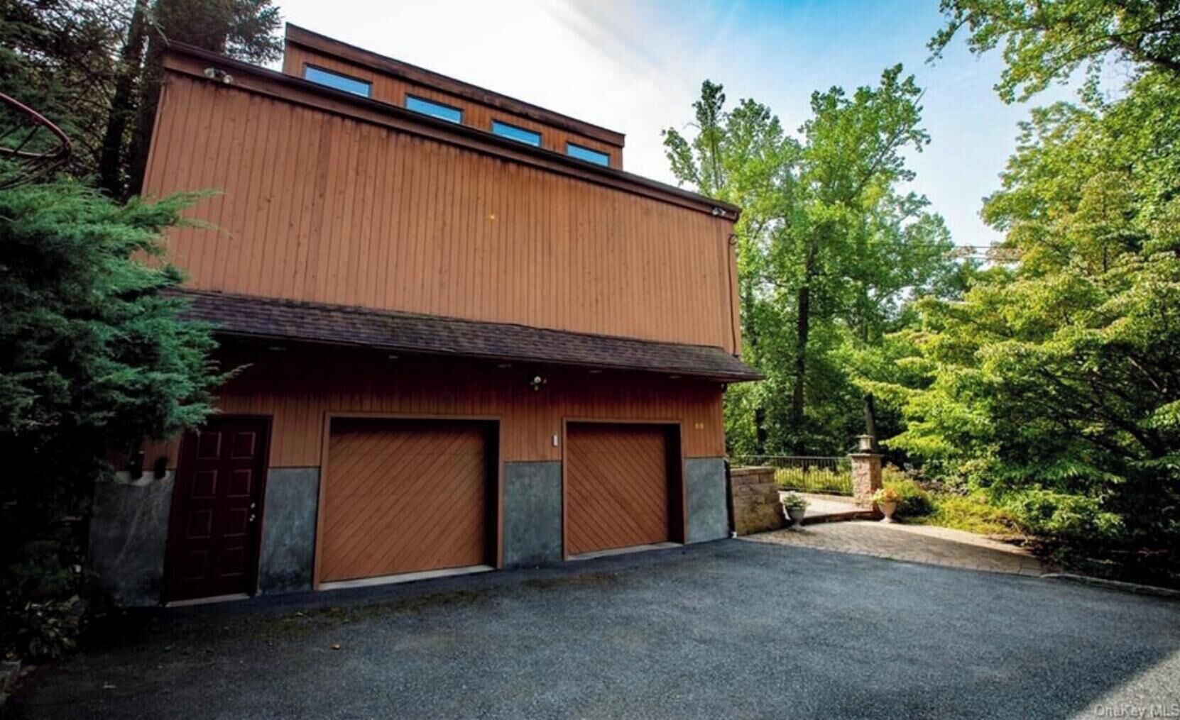 A two-story building with a wooden exterior, two garage doors, and a driveway.
