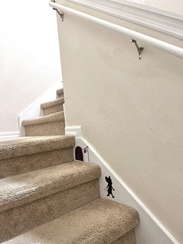 Una escalera con alfombra, barandilla y un pequeño acceso en la parte inferior.