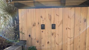 A wooden fence with two signs, a potted plant, and a wooden barrel.