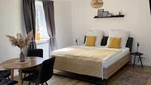 A modern bedroom with a wooden bed, a round dining table, and a large window with curtains.