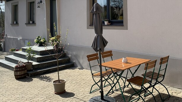 A house with a tiled roof, a patio with a table and chairs, and potted plants.