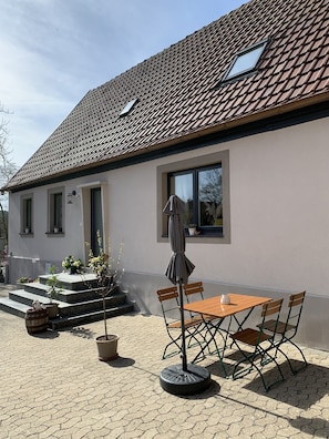 A house with a tiled roof, a patio with a table and chairs, and potted plants. - Vacation apartment I Beck-Bräu near Bamberg (Lisberg)