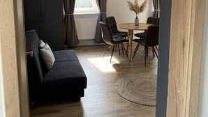 A modern living room with a dark sofa, a dining table with chairs, and a wooden ceiling.