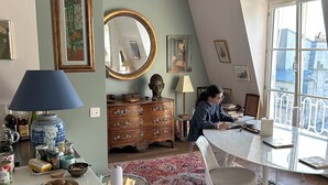 Un salon chaleureux comprenant un coin repas, une commode en bois et une grande fenêtre donnant sur la ville.