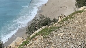 Une plage côtière avec un premier plan rocheux, une plage de sable et une chaîne de montagnes en arrière-plan.