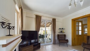 Un salon avec un téléviseur, une cheminée, un fauteuil et une porte donnant sur un balcon.