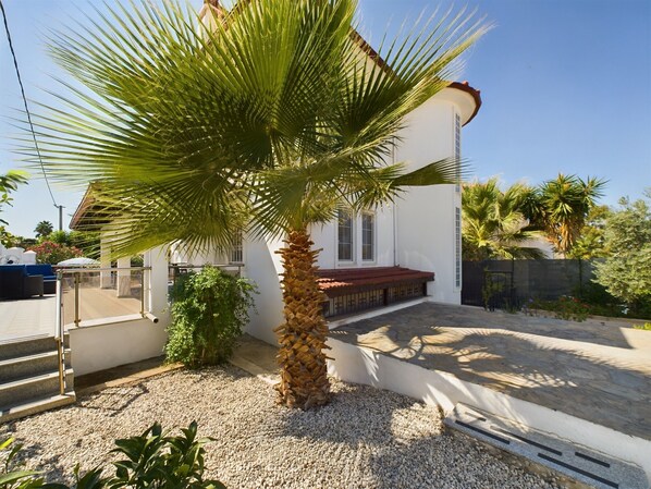 A modern house with a palm tree in the front yard, a white exterior, and a red roof.