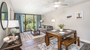 Un salon moderne avec un coin repas, de grandes fenêtres et un ventilateur de plafond.