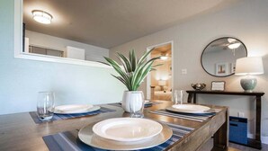 Un coin repas avec une longue table en bois, dressée pour quatre personnes, une plante en pot et un miroir au mur.