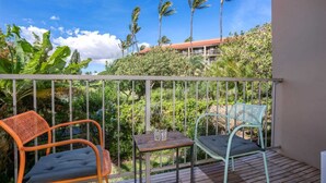 Un balcon avec deux chaises et une petite table, entouré d’une végétation luxuriante et de palmiers.