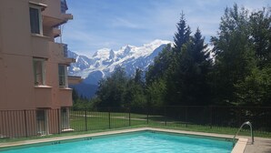 En swimmingpool med klart, blått vatten, omgiven av ett staket, och en byggnad med balkonger.