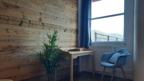Ett rum med träväggar, ett fönster med utsikt, ett litet bord, en stol och en krukväxt.