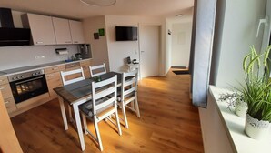 A modern kitchen with wooden cabinets, a built-in oven, and a dining area with white chairs and a table.
