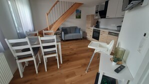 A compact living space with a dining area, a kitchenette, a gray sofa, and a wooden staircase.