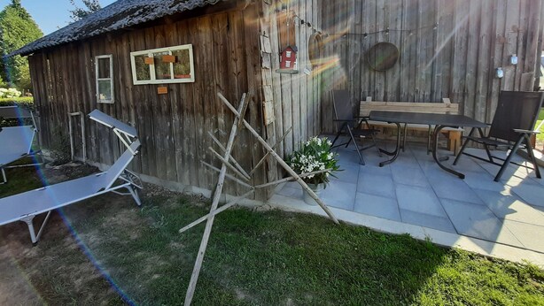 A rustic wooden building with a tiled roof, a small table with chairs, and a bench.