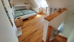 A loft bedroom with a bunk bed, a wooden floor, a chair, and a small table.