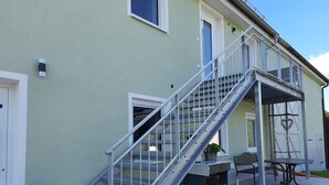 A two-story building with a metal staircase, a balcony, and a small outdoor seating area.
